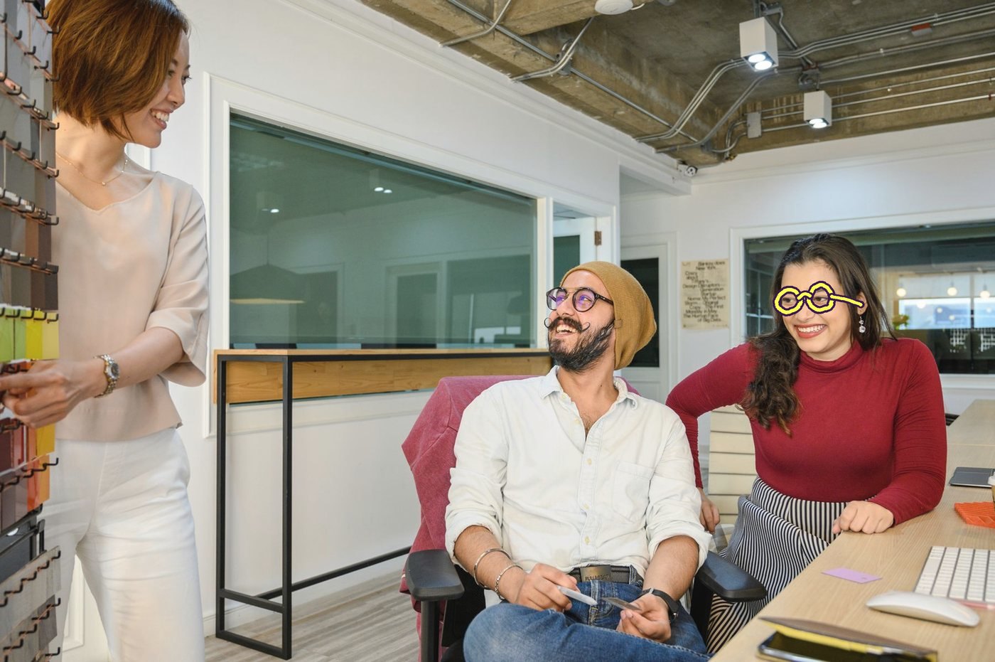 An agency team laughing together in an open office, the woman on the right in drawn lemon round glasses